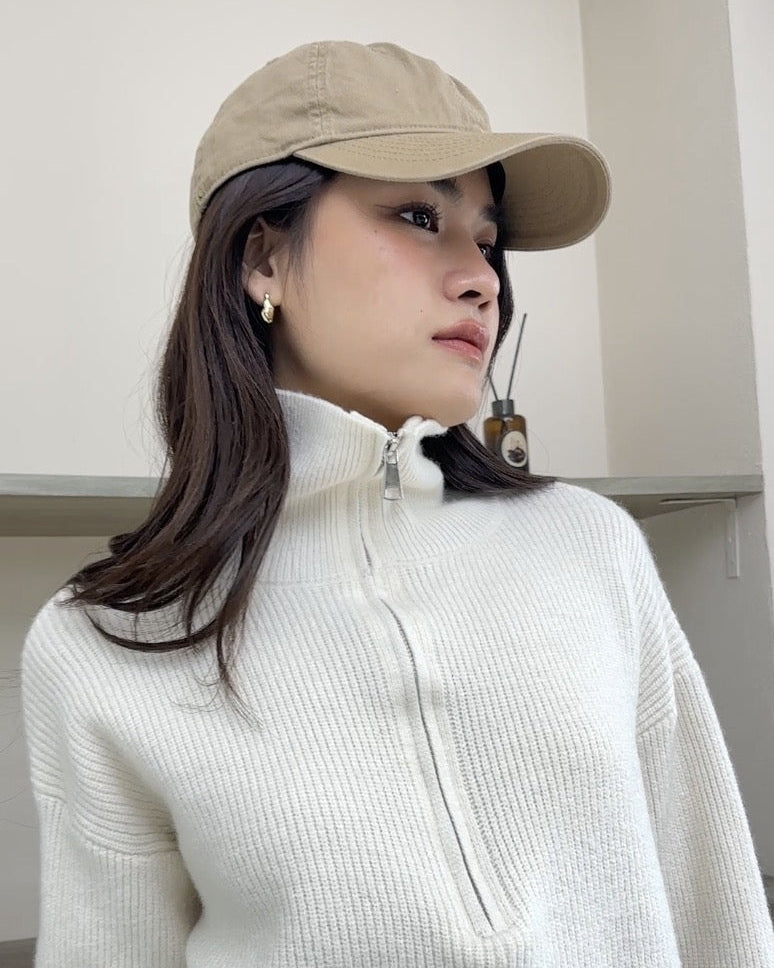 Woman wearing a beige cap and white high-neck sweater indoors