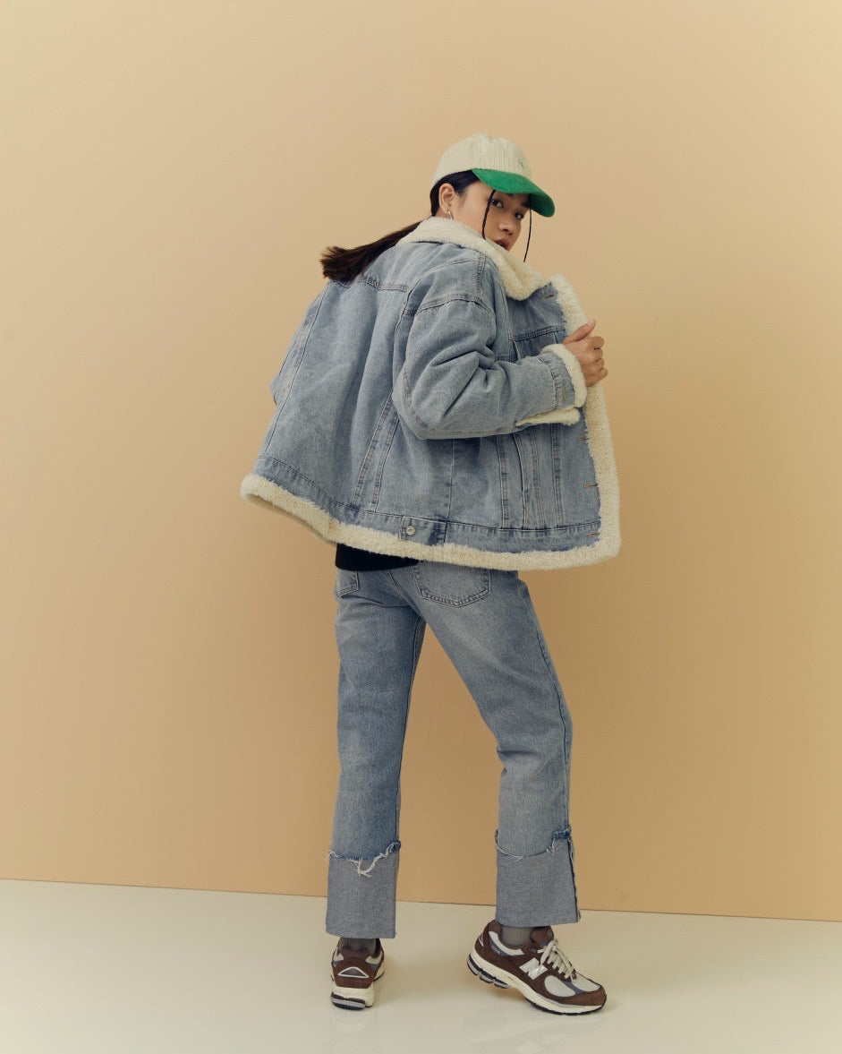 woman wearing a denim jacket, jeans, and sneakers against a beige background