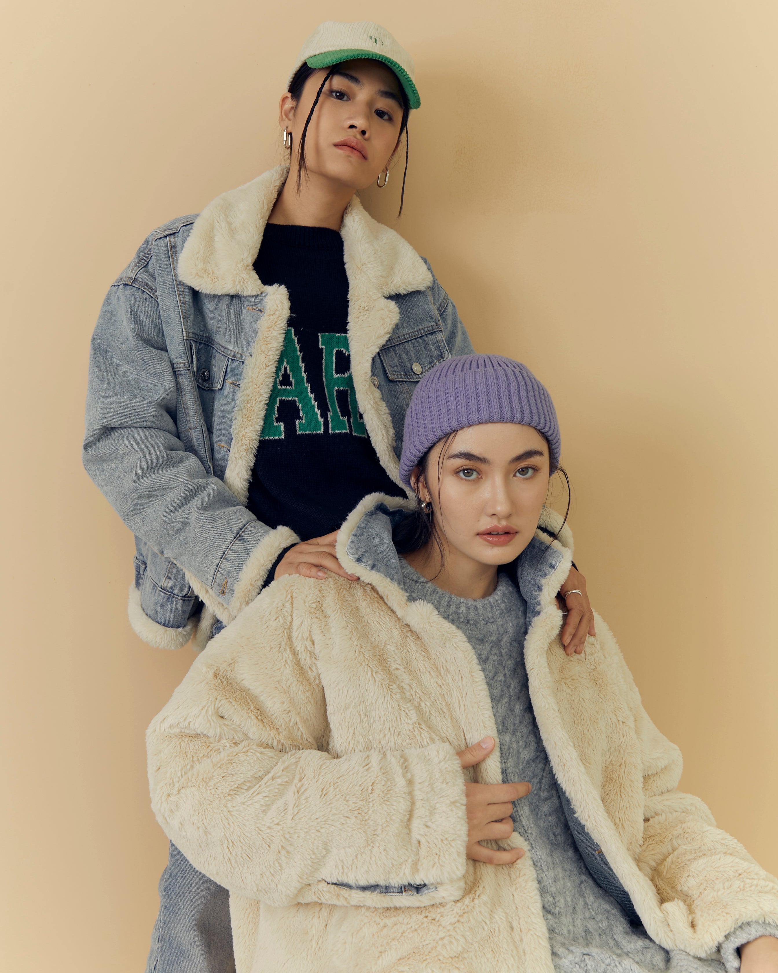 Two woman wearing stylish winter jackets and hats against a beige background