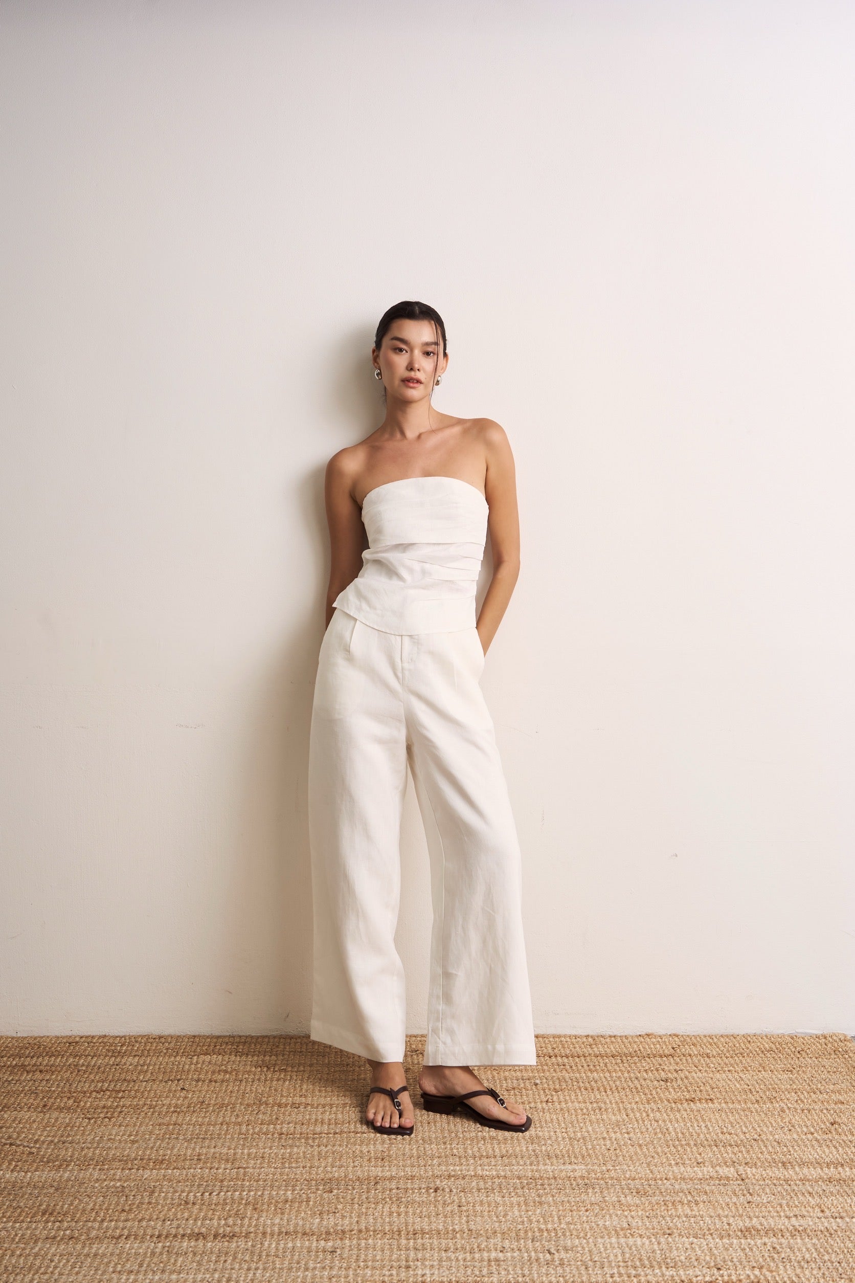 Woman wearing a white strapless linen top and white wide-leg linen pants against a plain background
