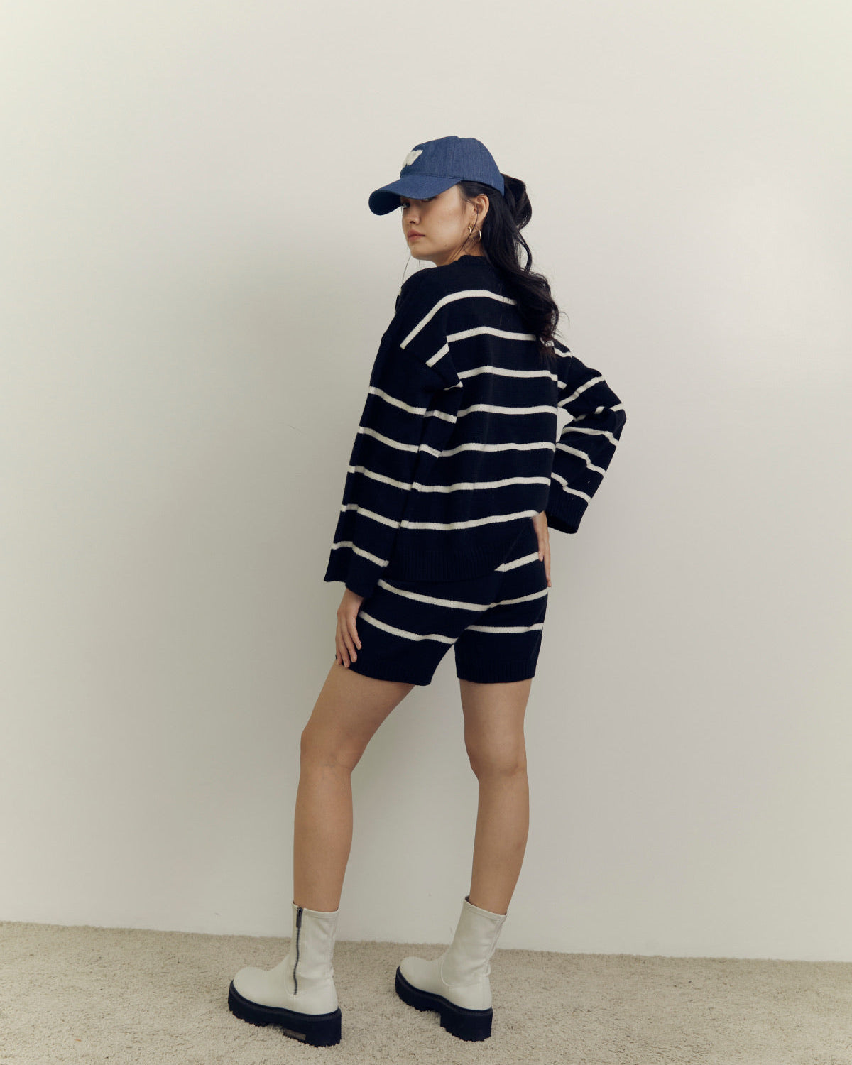 woman wearing a navy and white striped outfit with a cap against a plain background
