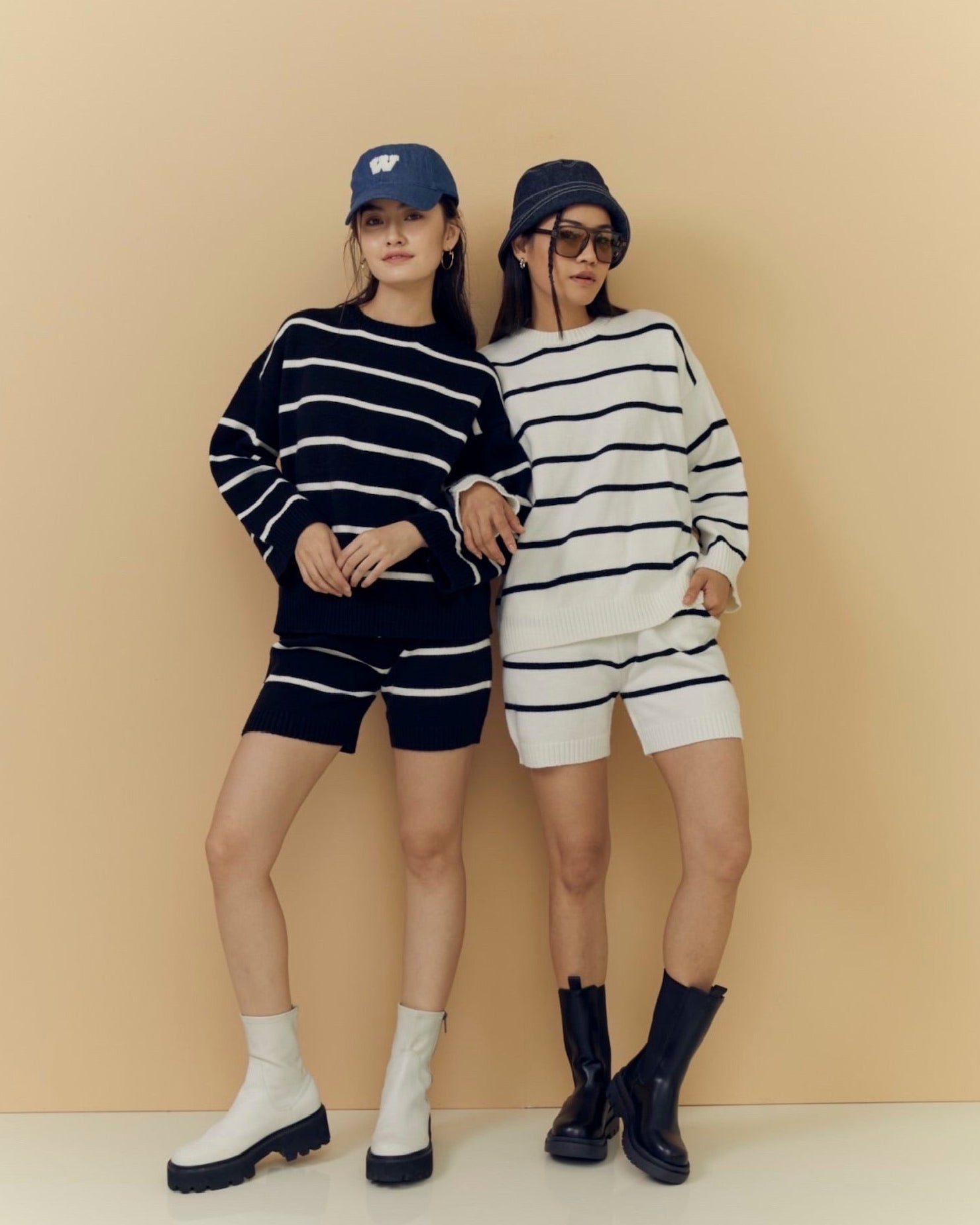 Two women wearing matching black and white striped outfits against a beige background