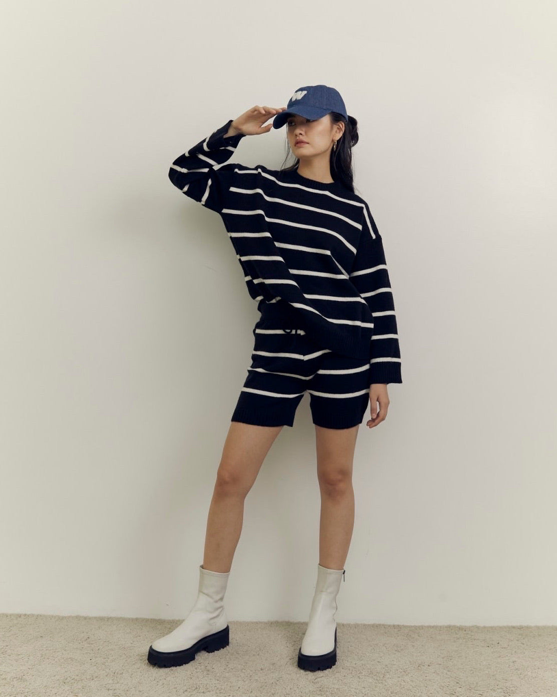 woman wearing a black and white striped outfit with a cap and boots on a plain background