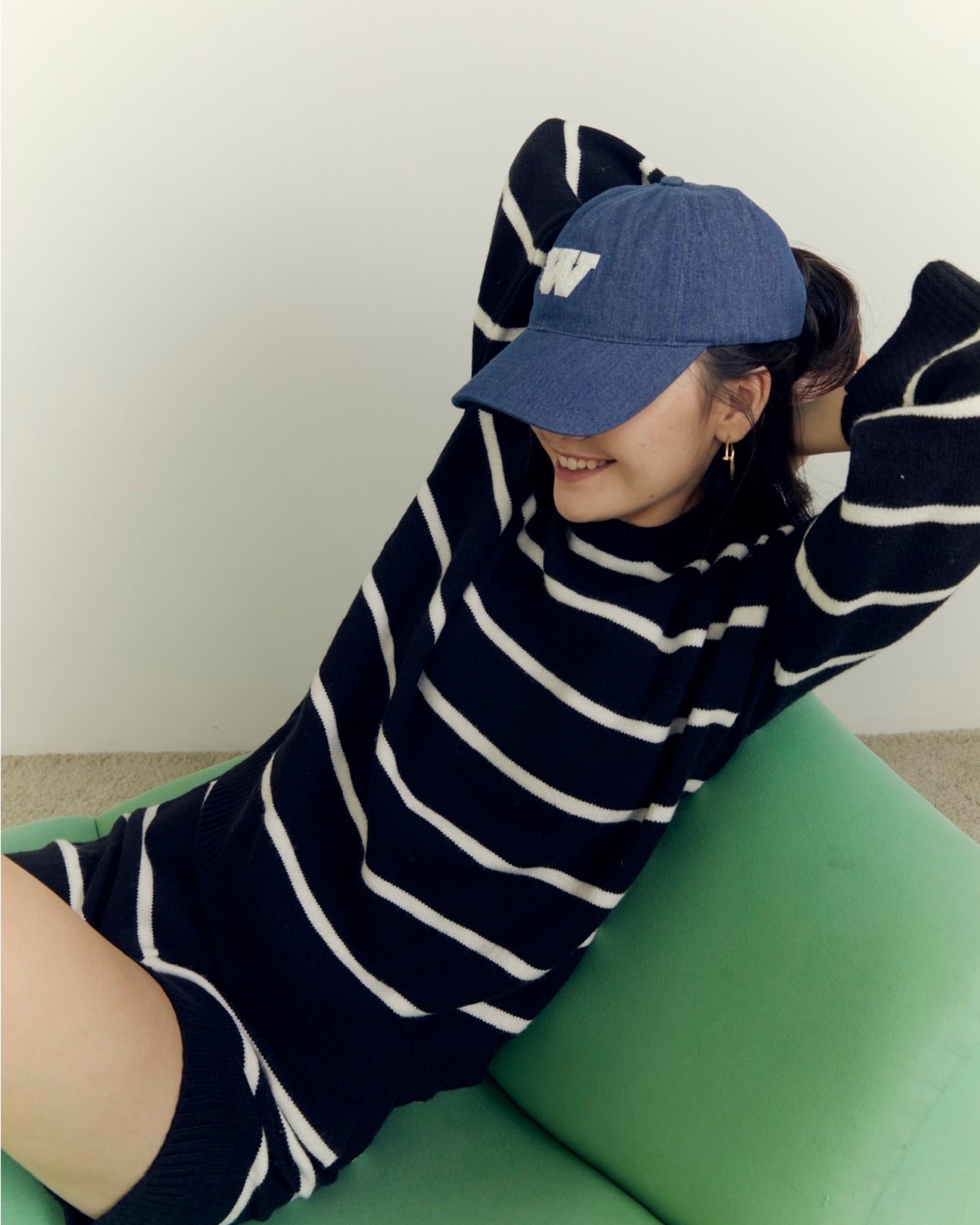 woman wearing a navy and white striped dress and blue cap sitting on a green couch.