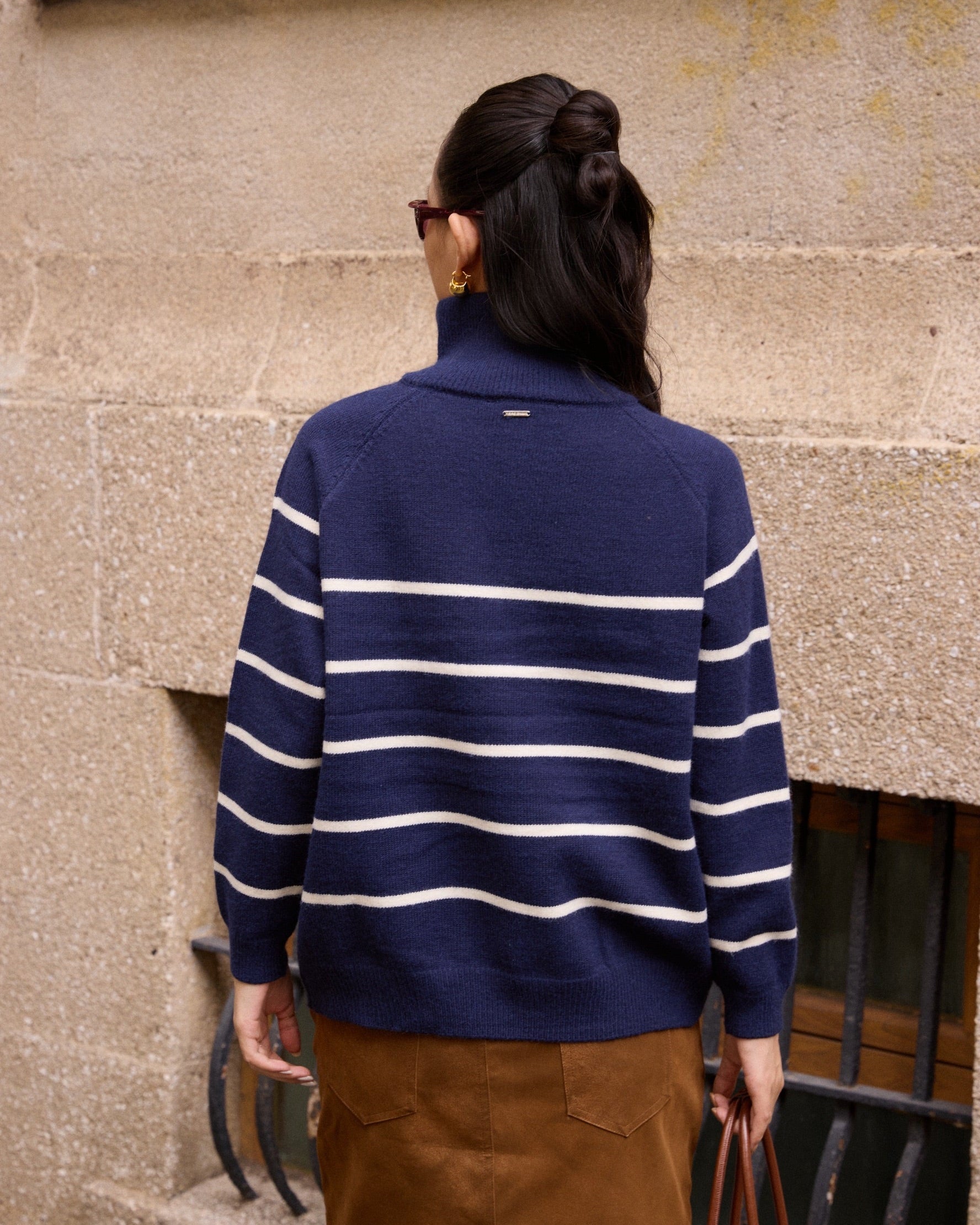 woman wearing a blue and white striped sweater standing against a textured wall.