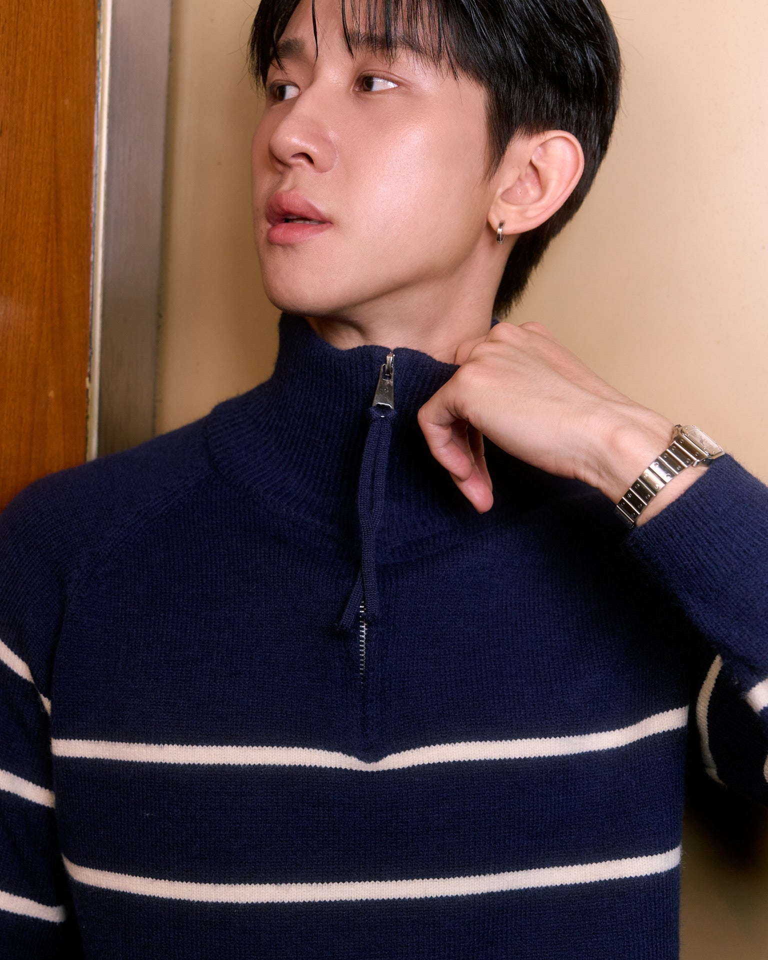 man wearing a navy blue sweater with white stripes, adjusting their collar indoors.