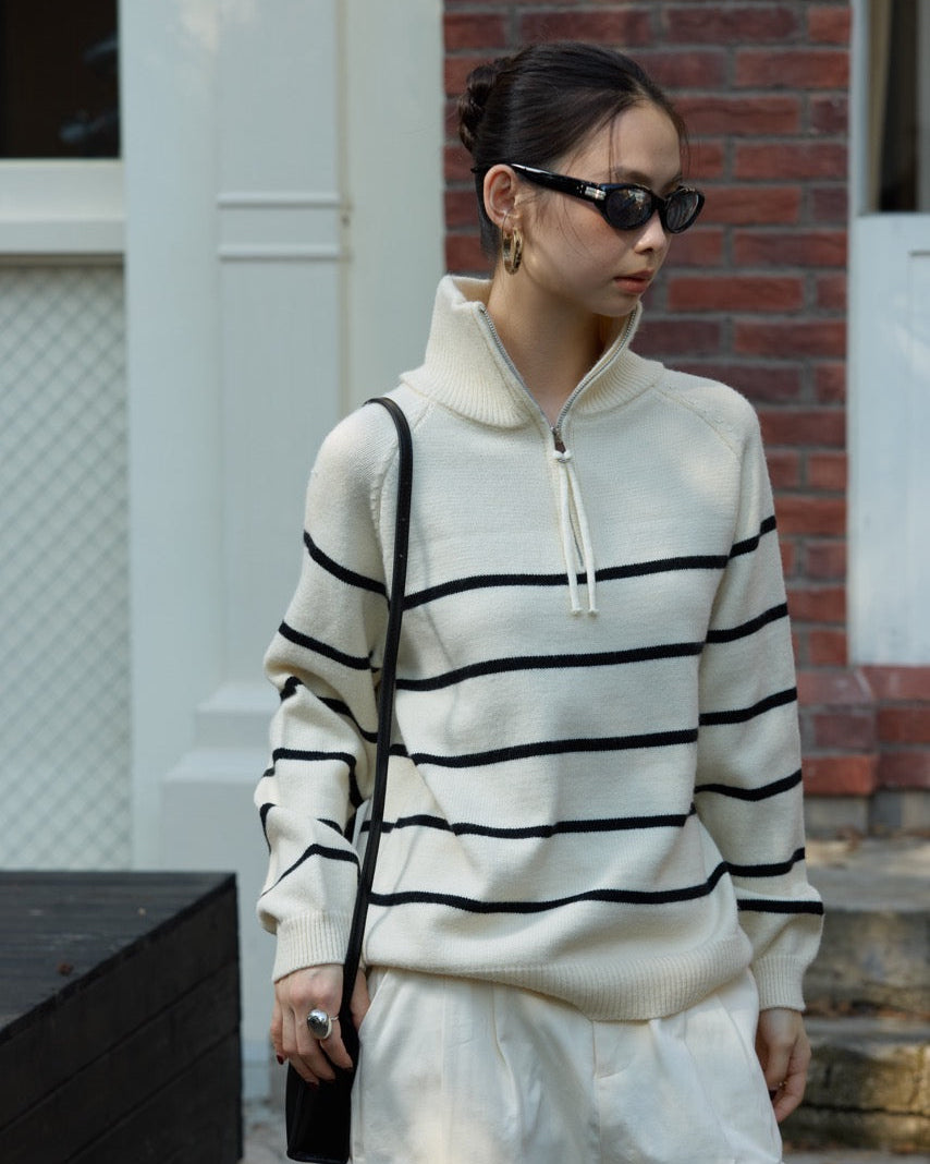 woman wearing a white and black striped sweater with a plain background
