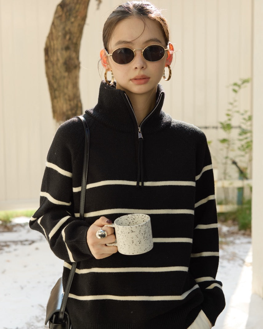 Woman wearing a black and white striped sweater holding a mug outdoors.