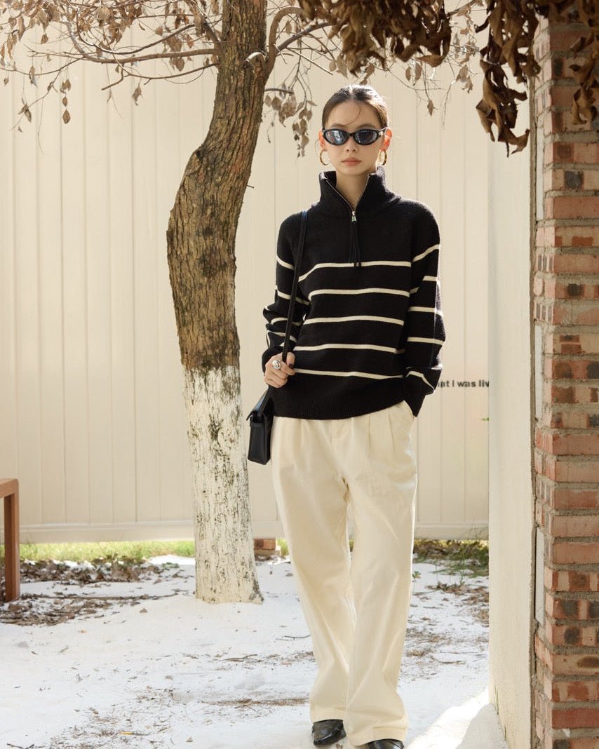 woman wearing a black and white striped sweater and beige pants standing outdoors.