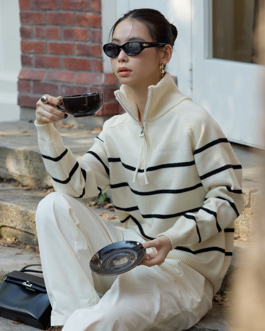 Woman in a striped sweater and white pants sitting on steps, holding a cup and saucer.