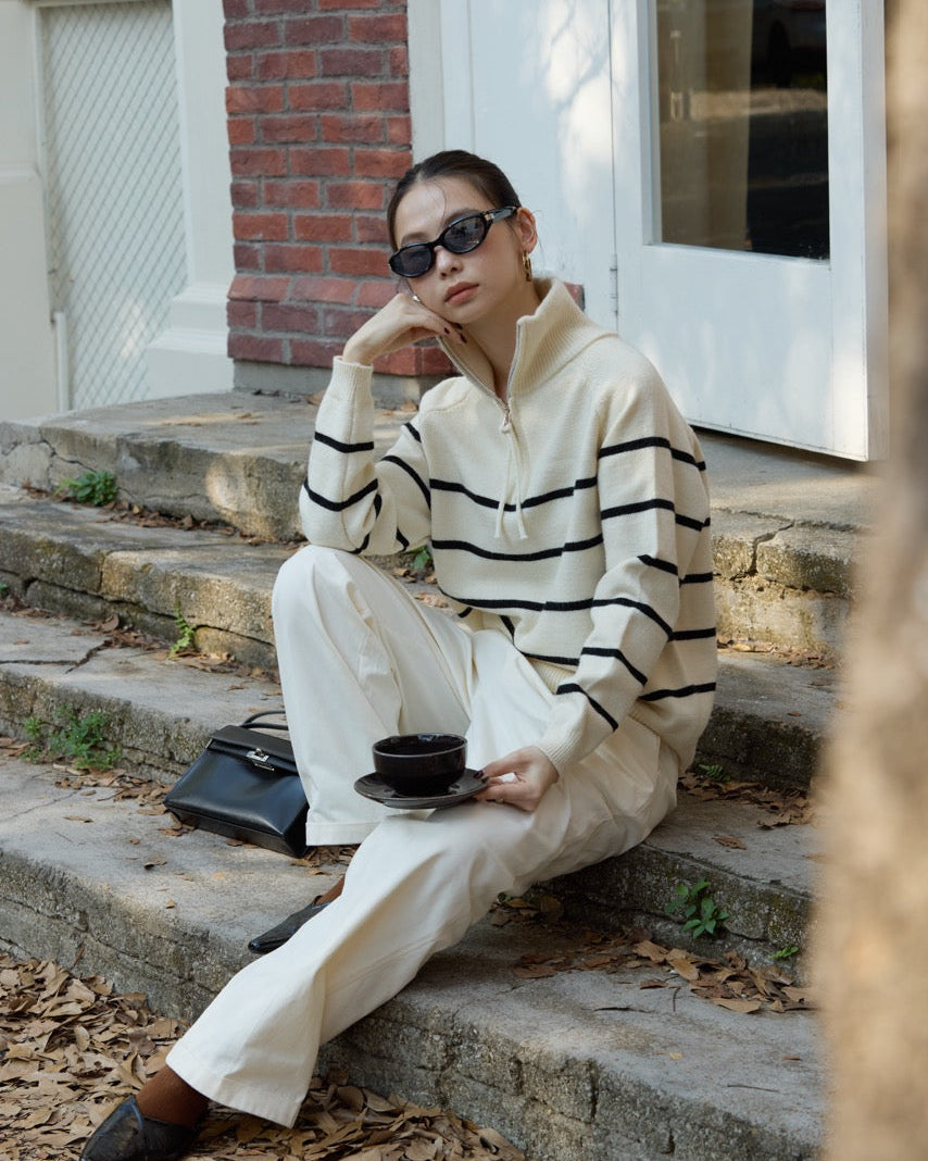 woman sitting on steps wearing a striped sweater and sunglasses, holding a cup.