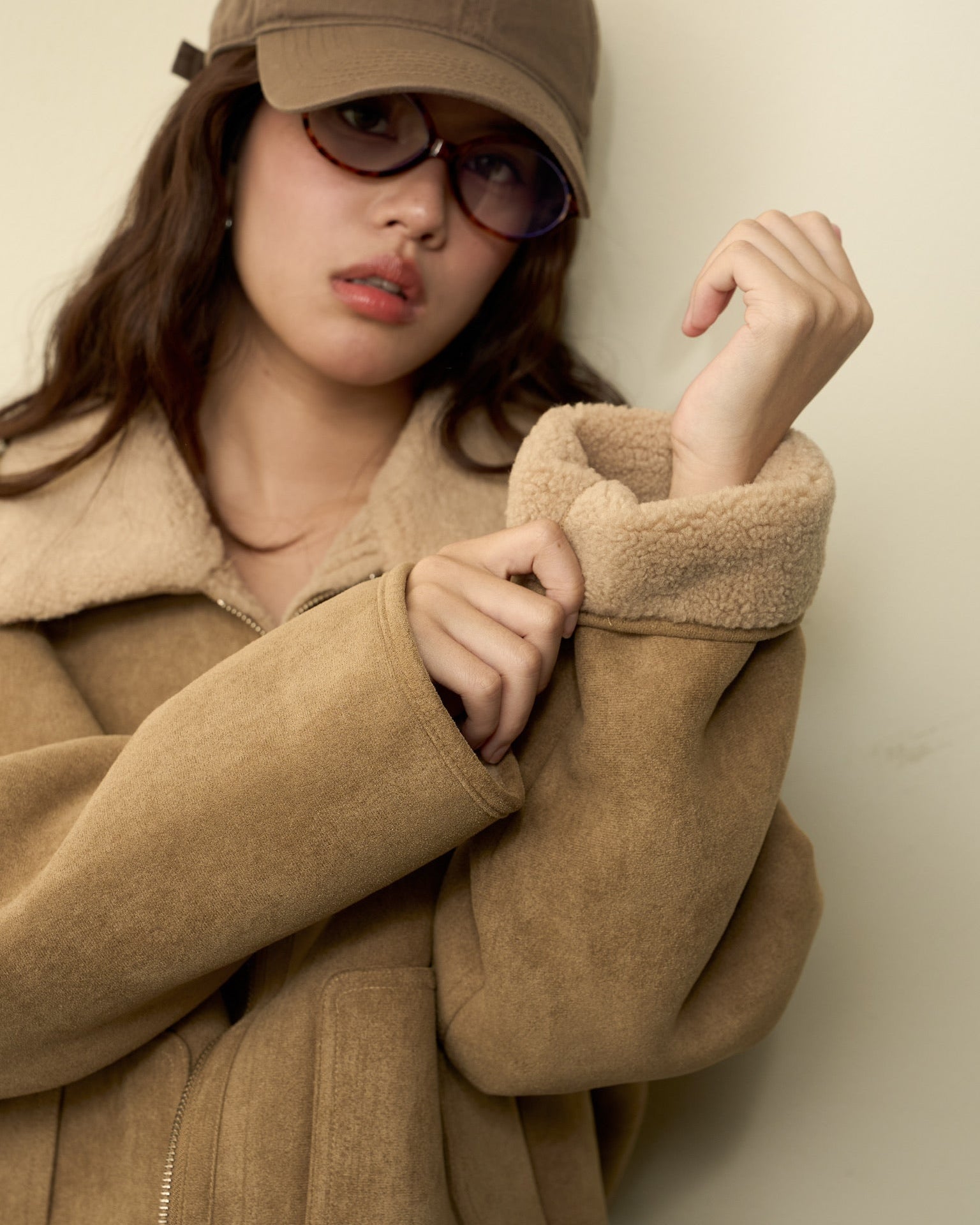 Woman wearing a beige coat and cap against a plain background