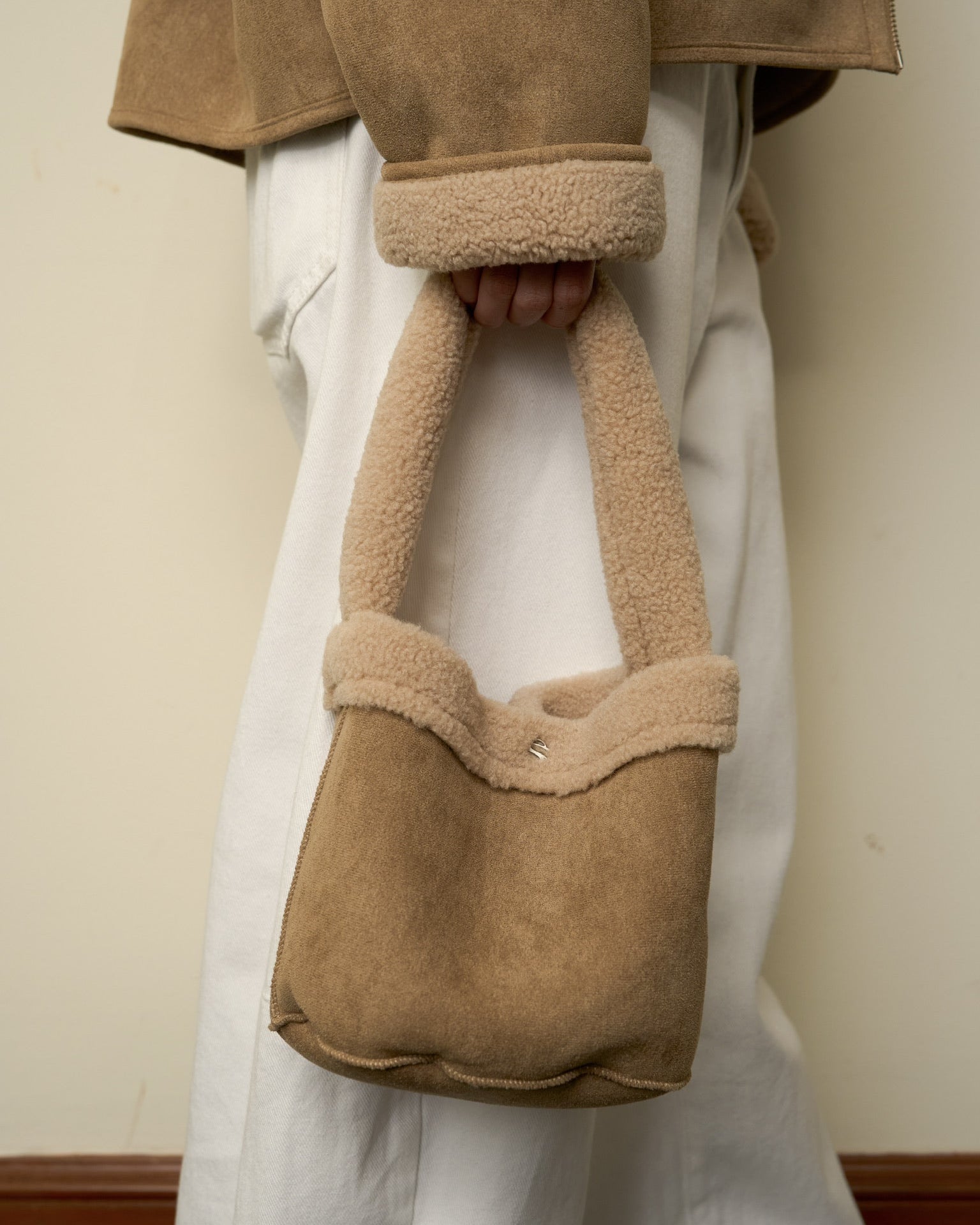 woman holding a brown suede handbag with fur trim against a plain background