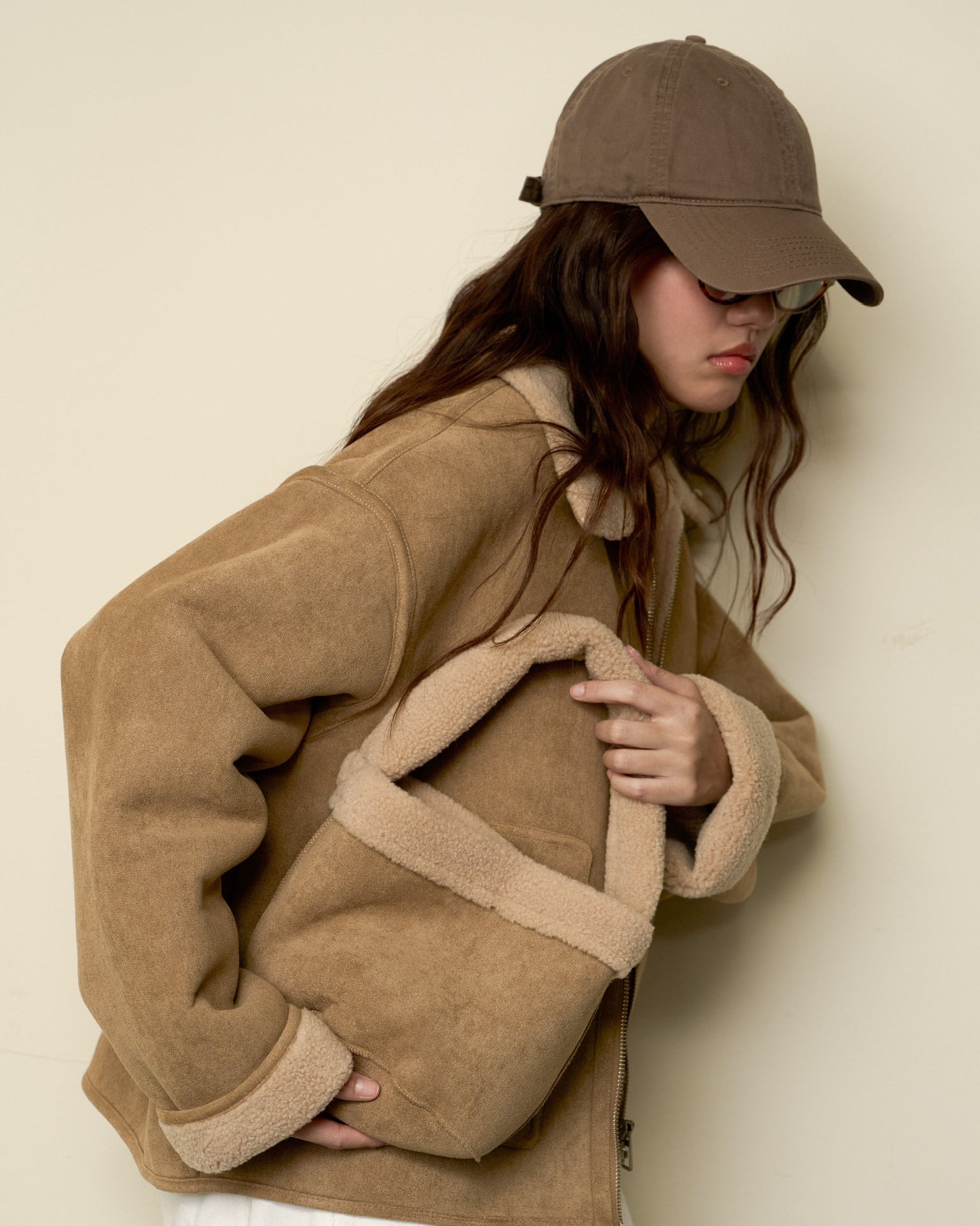 woman wearing a brown jacket and cap against a beige background