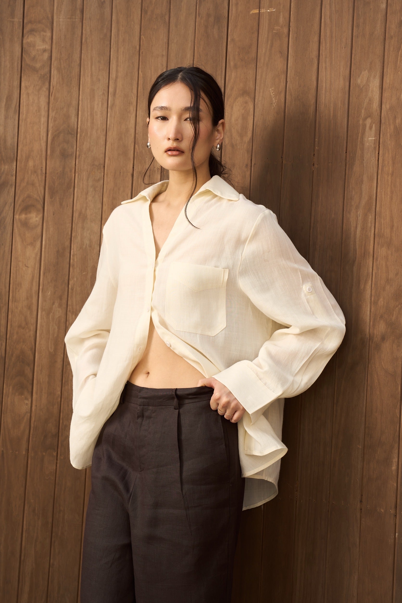 Woman wearing a yellow linen shirt and dark pants against a wooden wall