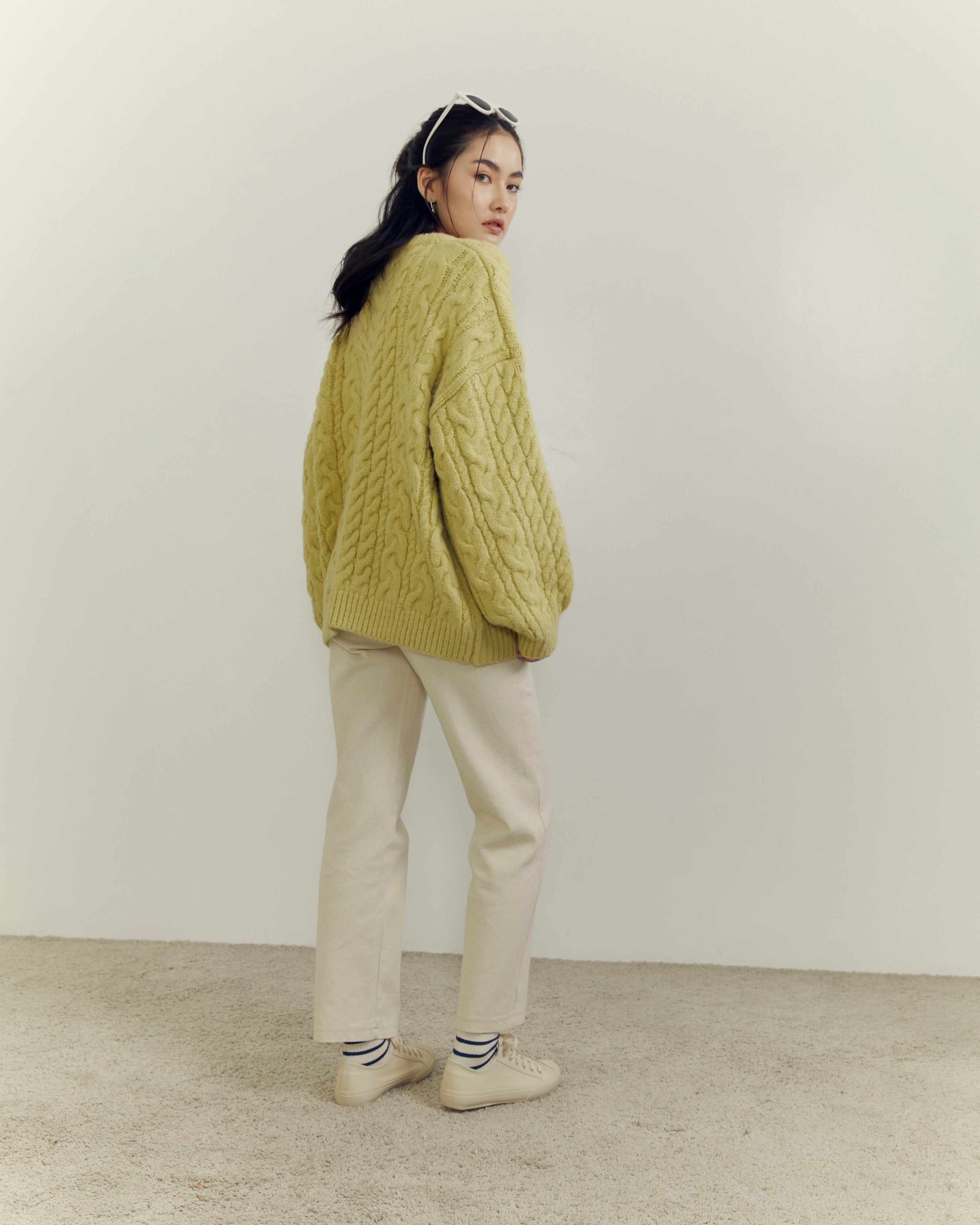 woman wearing a green knitted sweater and beige pants against a white background
