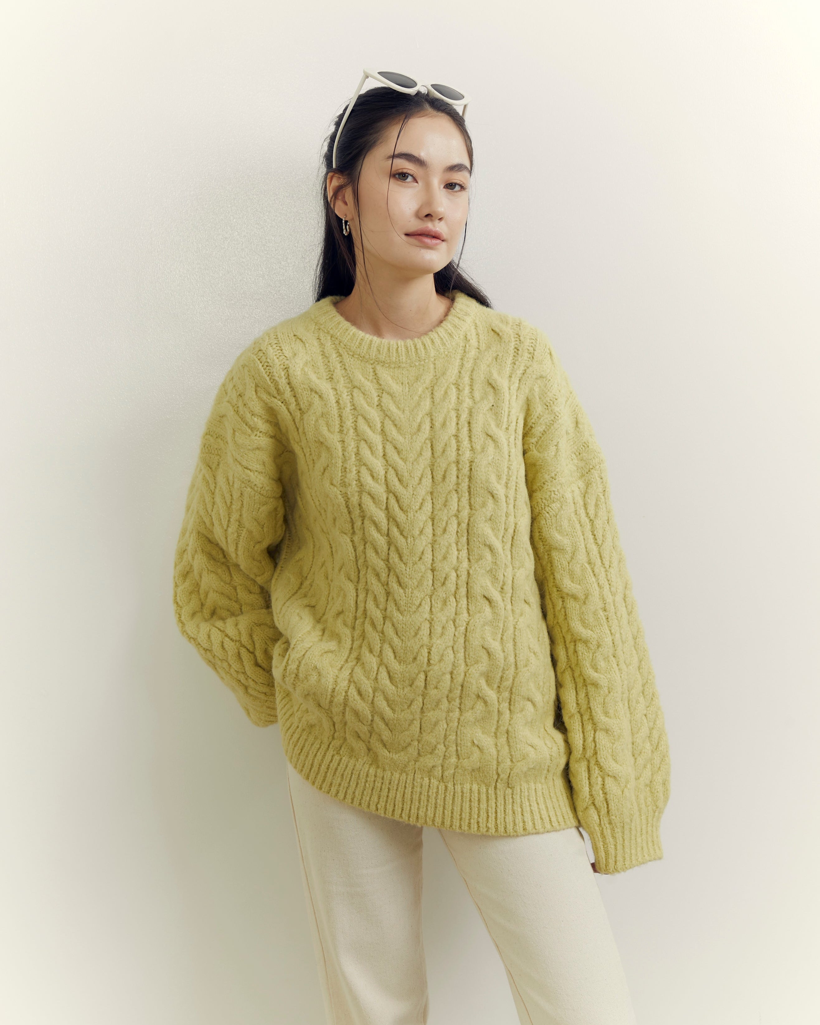 Woman wearing a green cable knit sweater against a white background