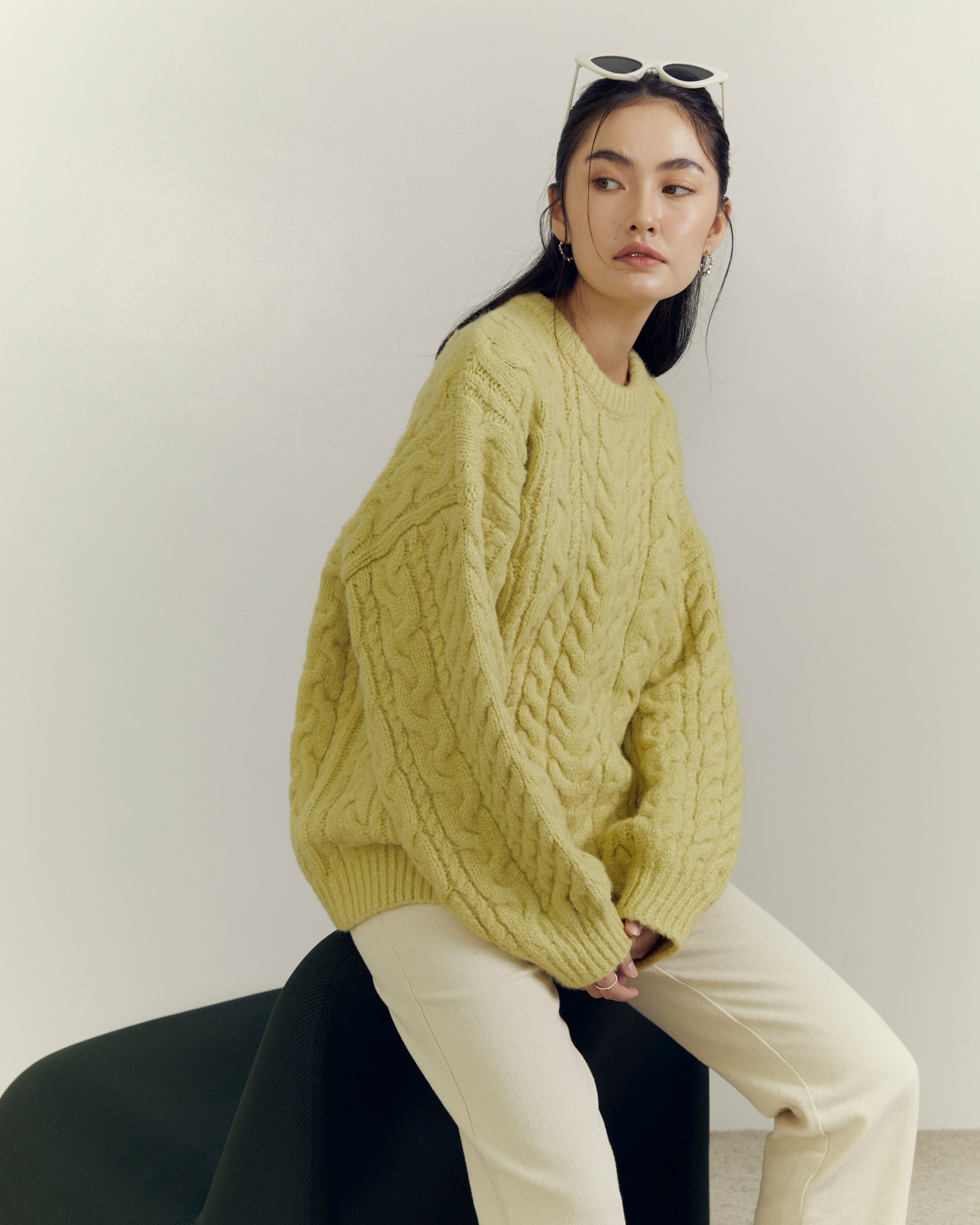 woman wearing a yellow sweater sitting on a black chair against a white wall