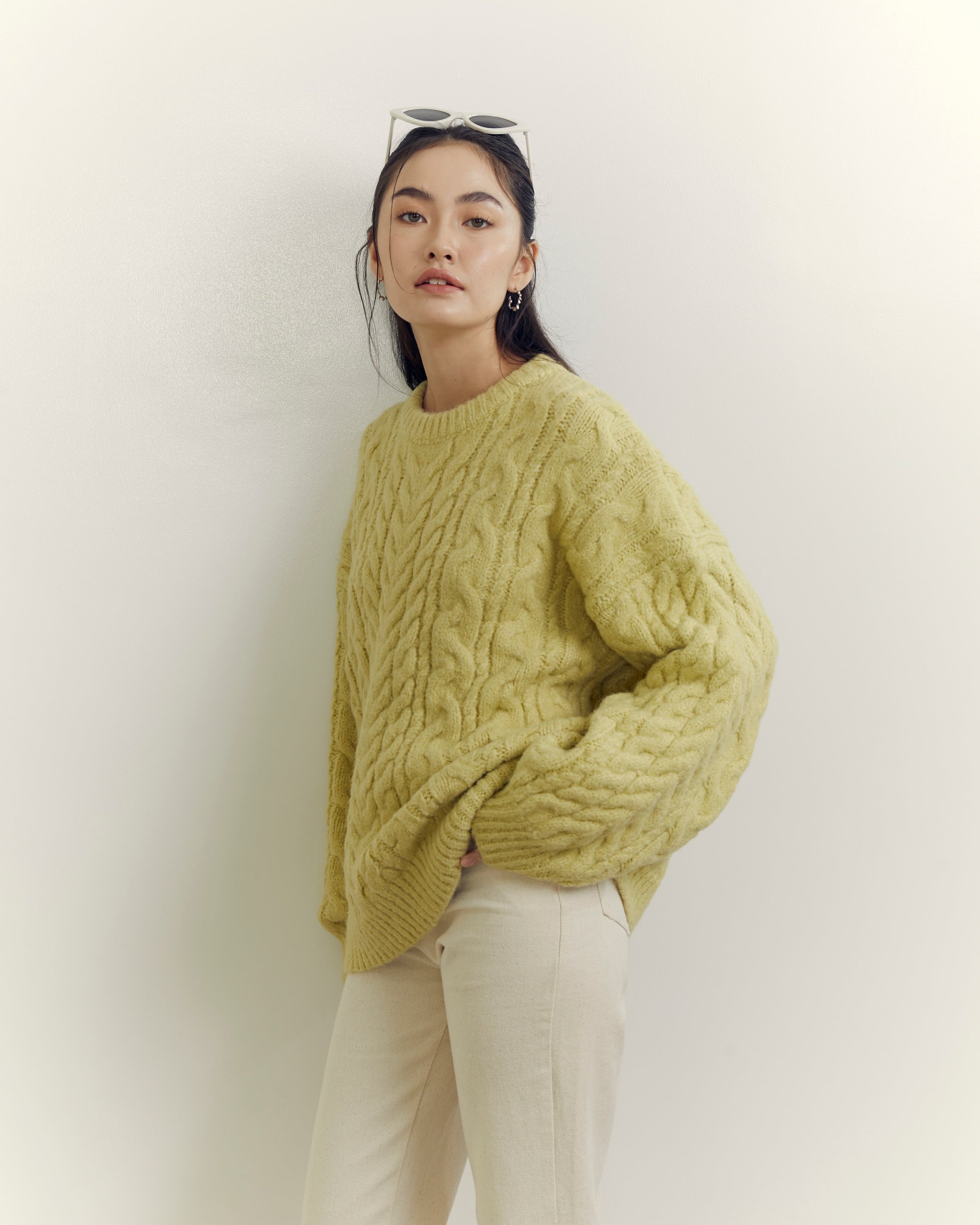 woman wearing a green cable knit sweater against a white background