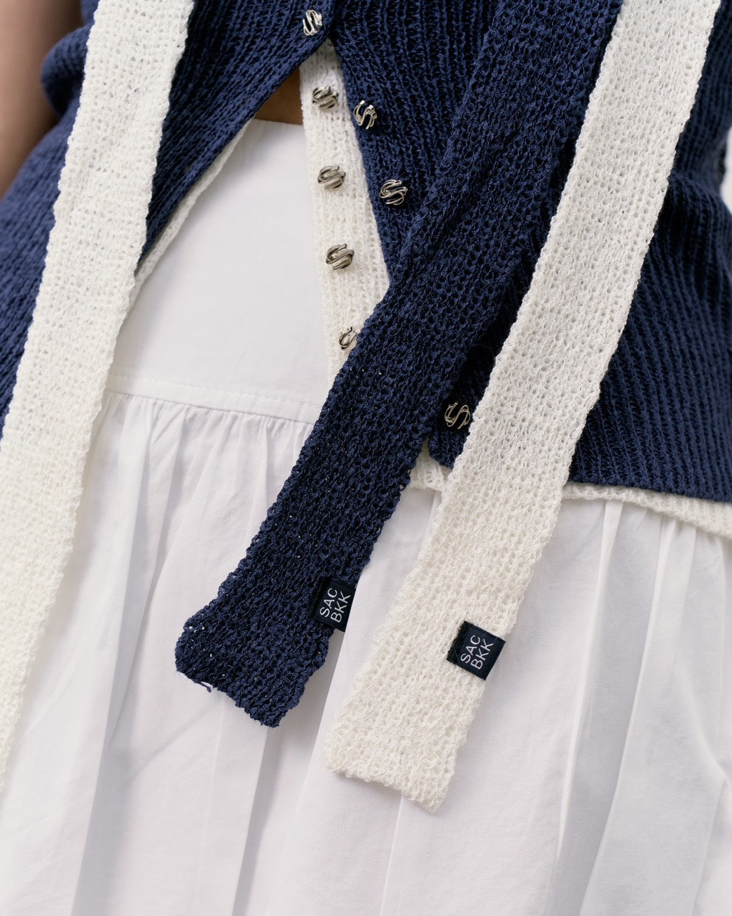 Close-up of a navy blue knitted cardigan with white trim and silver buttons, worn over a white dress.