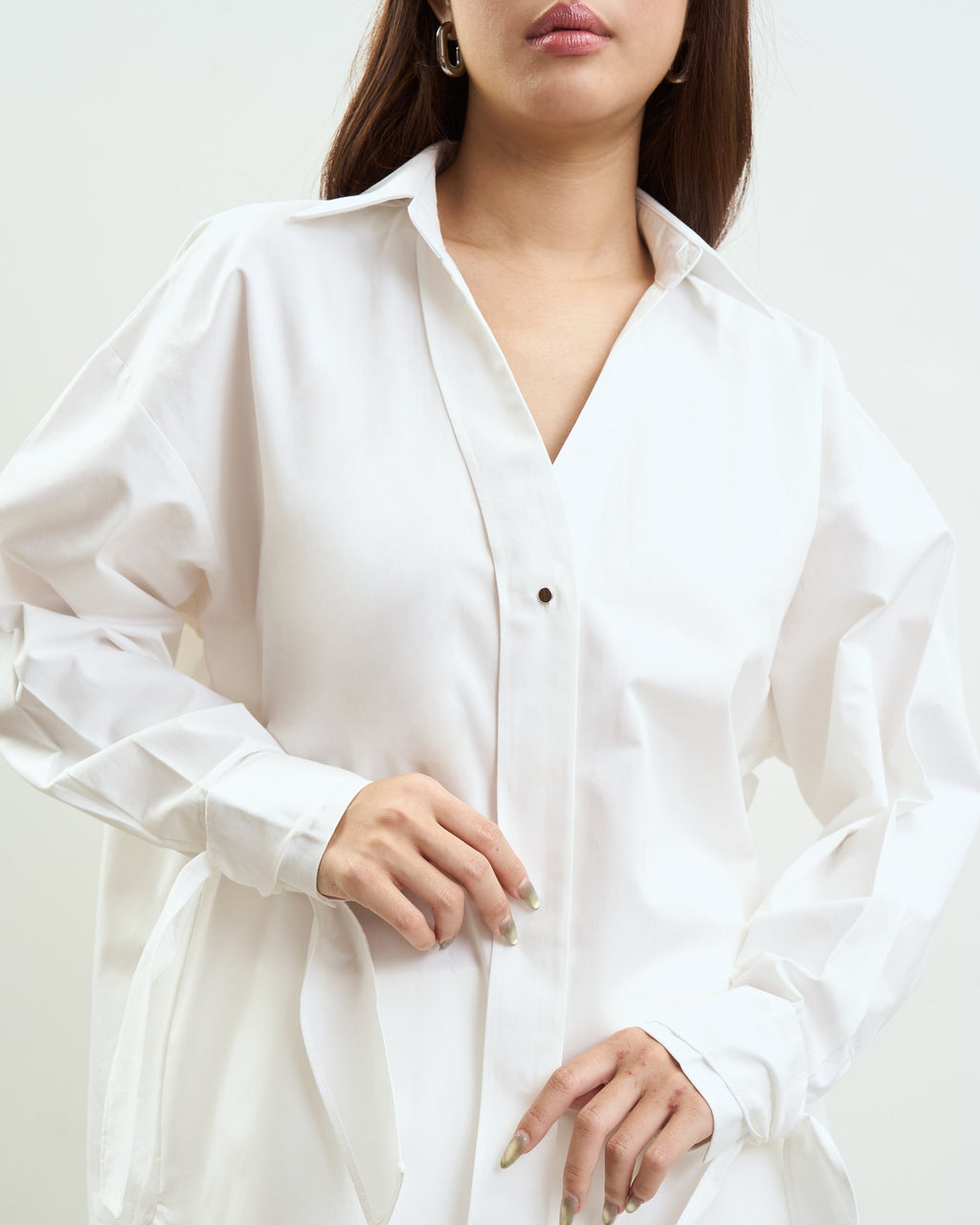 woman wearing an oversized white button-up shirt with long sleeves and a relaxed fit, shown from the shoulders to the hips against a plain light background.