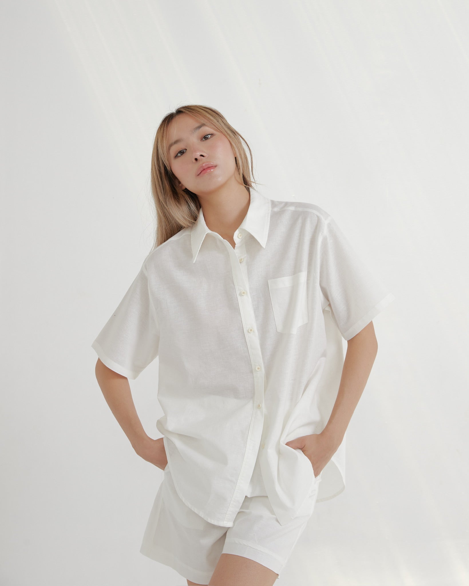 woman wearing a white oversized shirt and shorts on a plain background